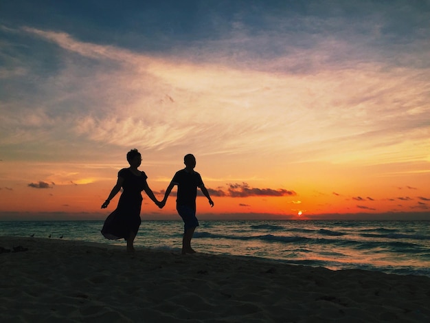 Couple de silhouettes se promenant sur la plage au coucher du soleil