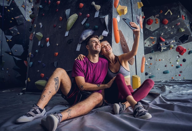 Un couple solide d'alpinistes contre un mur artificiel avec des poignées et des cordes colorées