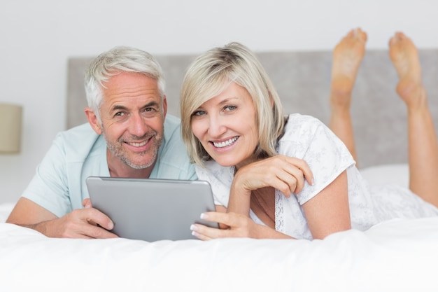 Couple souriant à l&#39;aide de tablette numérique dans son lit