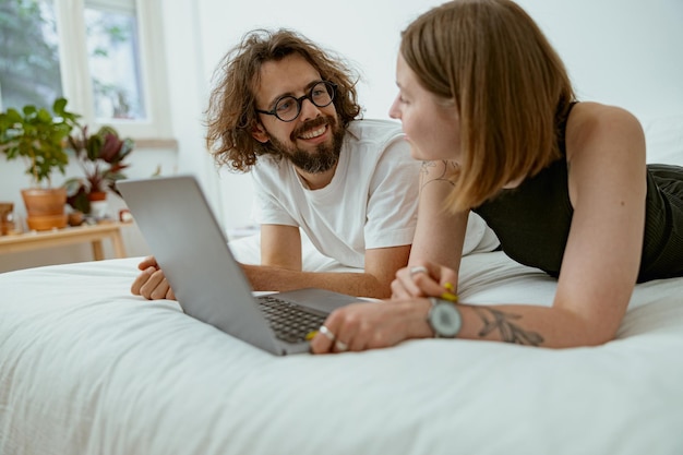 Couple souriant allongé dans son lit ensemble tout en regardant un film ou une vidéo en ligne à leur temps familial à la maison