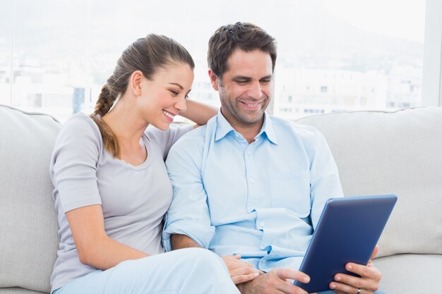 Couple souriant, assis sur le canapé à l&#39;aide de tablet pc