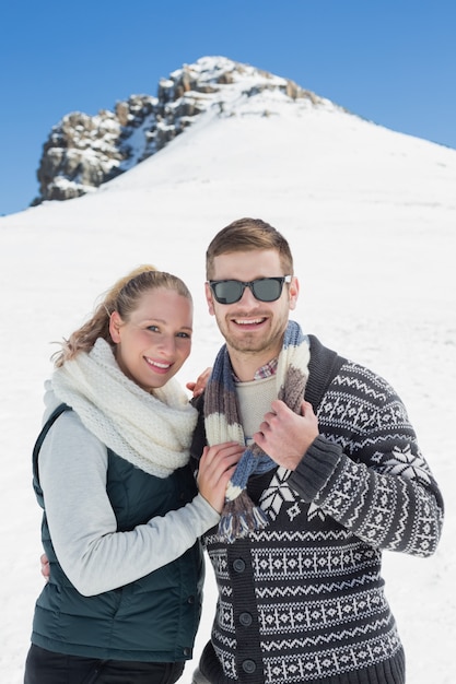Couple souriant dans des vêtements chauds en face de la colline enneigée