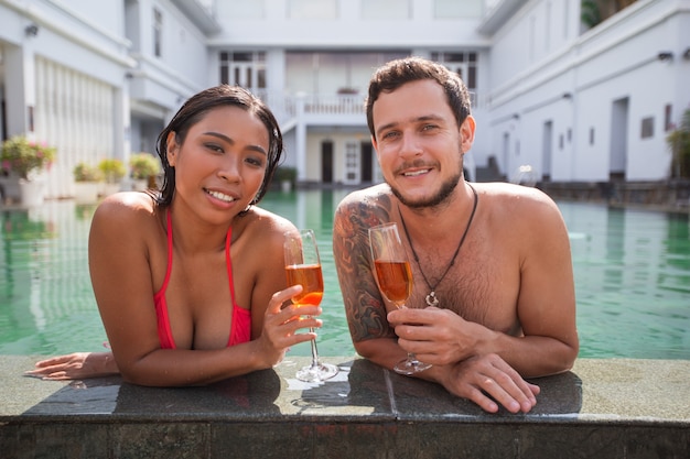Couple souriant avec du champagne au bord de la piscine