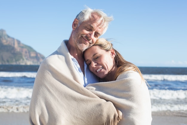 Couple souriant enveloppé dans une couverture sur la plage