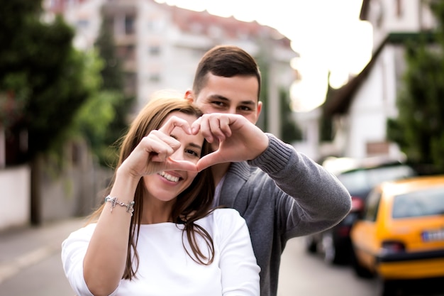 Couple souriant formant une forme de coeur avec leurs mains à la rue