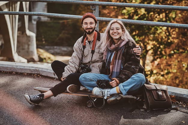 Un couple souriant et heureux se détend sur un longboard avec des arbres dorés à l'arrière-plan.