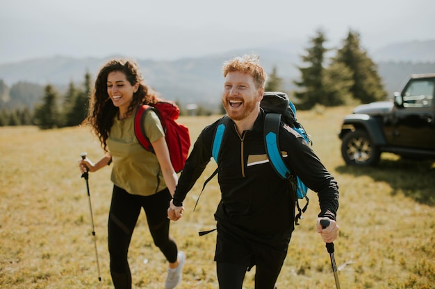 Photo couple souriant marchant avec des sacs à dos sur les collines vertes