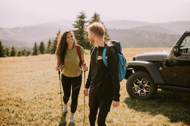 Couple souriant marchant avec des sacs à dos sur les collines vertes