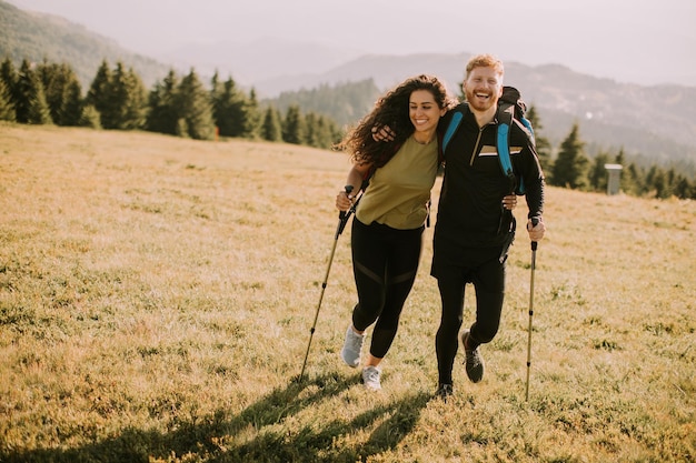 Couple souriant marchant avec des sacs à dos sur les collines vertes