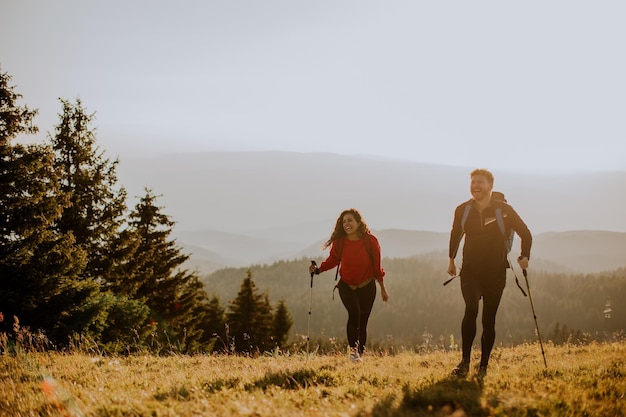 Couple souriant marchant avec des sacs à dos sur les collines vertes