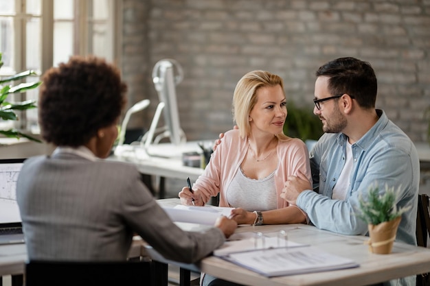 Photo couple souriant parlant pendant que la femme signe un contrat lors de la rencontre avec l'agent d'assurance au bureau