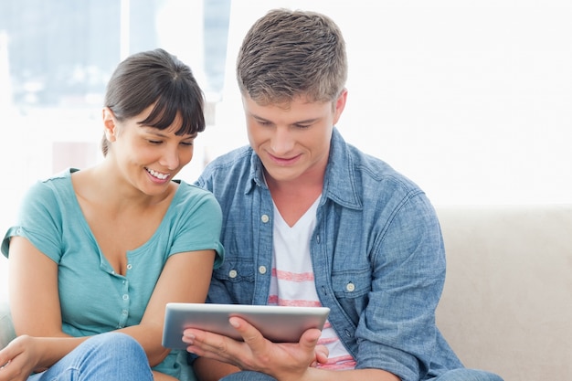 Un couple souriant s&#39;asseoir sur le canapé et utiliser une tablette