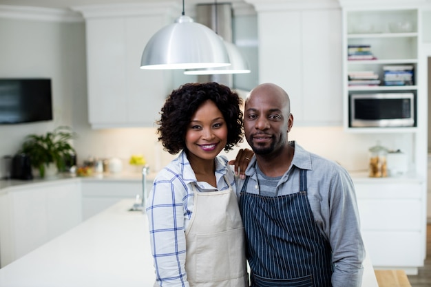 Couple souriant en tablier debout à la cuisine