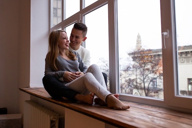 Couple souriant tout en étant assis près de la fenêtre à la maison