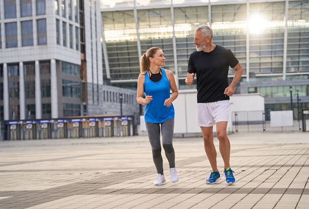 Couple sportif d'âge moyen homme et femme en tenue de sport discutant en faisant du jogging ensemble à l'extérieur