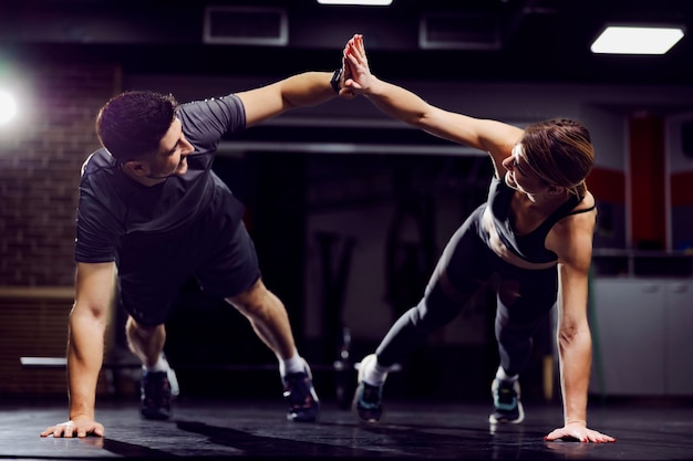 Un couple sportif en forme qui se donne un high five tout en faisant des planches et des exercices dans une salle de sport