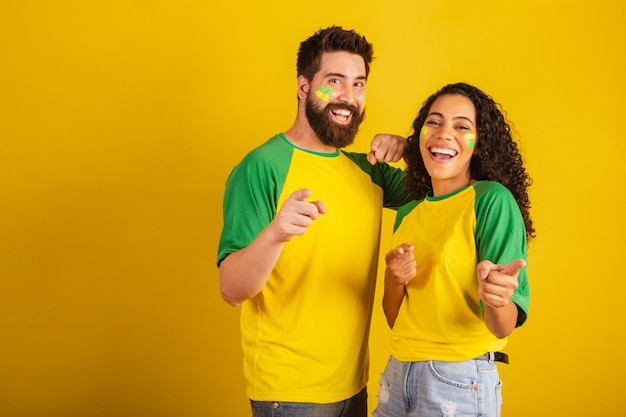 Couple de supporters de football brésiliens vêtus aux couleurs de la nation femme noire homme caucasien pointant vers la caméra