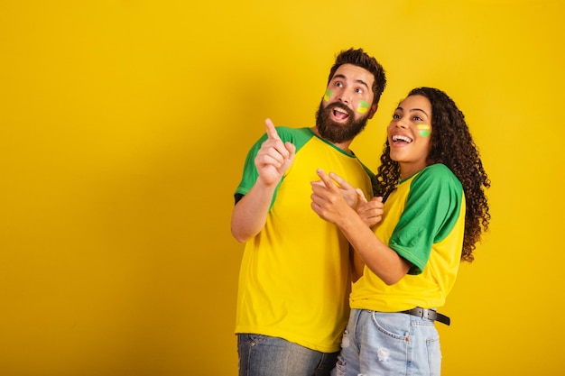 Couple de supporters de football brésiliens vêtus aux couleurs de la nation femme noire homme caucasien pointant vers la caméra