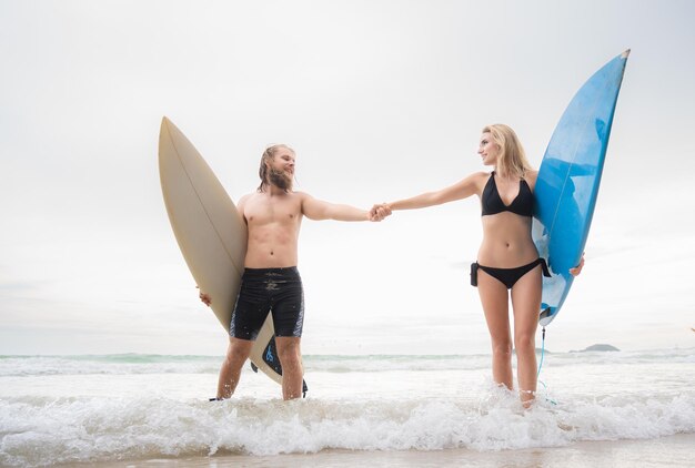 Un couple de surfeurs se tenant par la main et se regardant sur la plage.