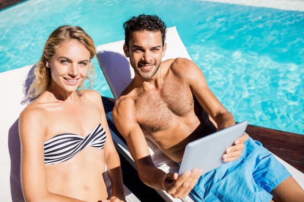 Couple avec tablette sur les transats au bord de la piscine