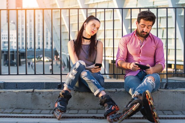 Un couple avec des téléphones est assis une femme ennuyée regardant un homme à qui vous envoyez des SMS