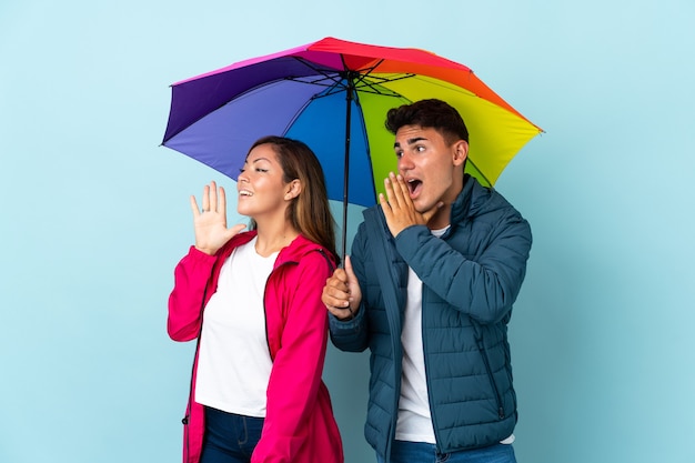 Couple tenant un parapluie bleu criant avec la bouche grande ouverte sur le côté