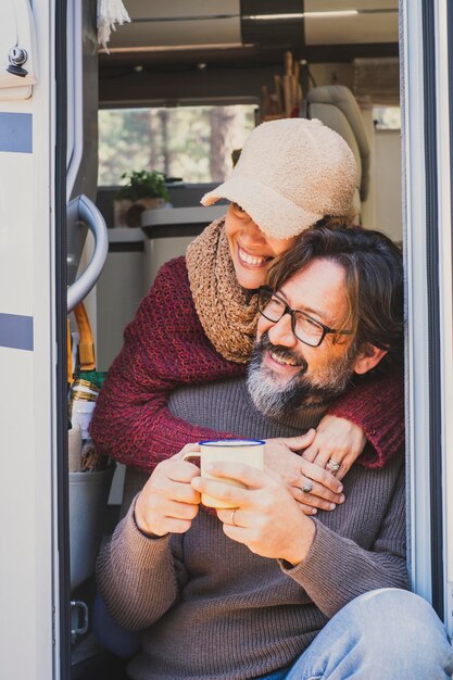 Couple de touristes adultes heureux assis sur la porte du camping-car admirant l'extérieur