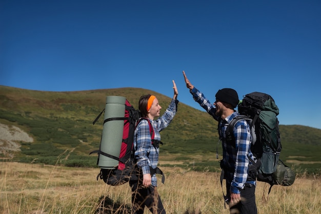 Un couple de touristes amoureux, un homme et une femme debout sur une plaine de montagne lèvent la main