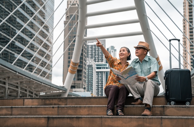 Un couple de touristes asiatiques âgés visitant la capitale avec bonheur et s'amusant et en regardant la carte pour trouver des endroits à visiter.