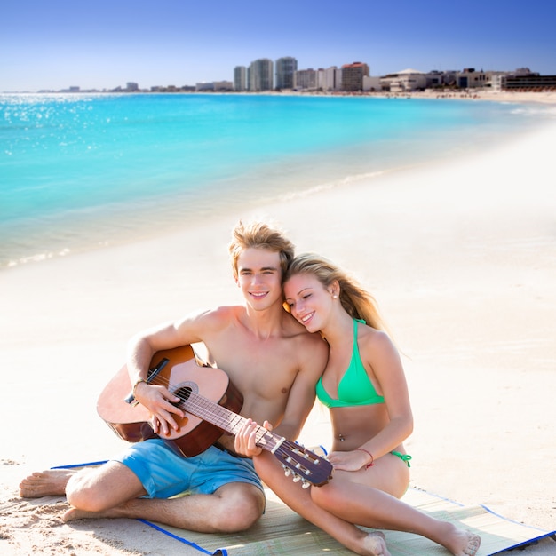 Couple de touristes blond jouant de la guitare sur la plage