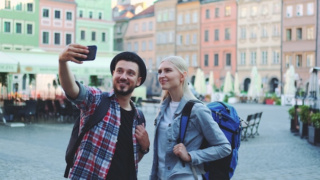 Couple de touristes faisant selfie sur smartphone dans le centre-ville. Ils ont des sacs de touristes.