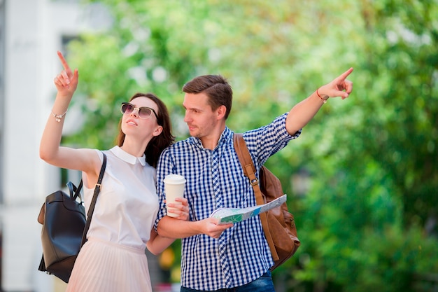 Couple de touristes heureux voyageant en Europe souriant heureux. Amis caucasiens avec carte de la ville à la recherche d'attractions. Jeune homme avec café chaud et belle femme avec une grande carte