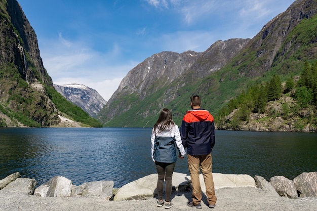 Couple de touristes méconnaissable, les bras levés, le dos tourné au pied du fjord et entouré de hautes montagnes à Gudvangen Norvège