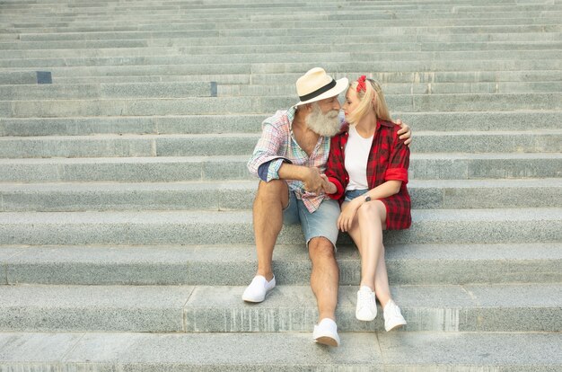 Couple de touristes romantiques assis dans les escaliers. Homme senior barbu et jeune femme.