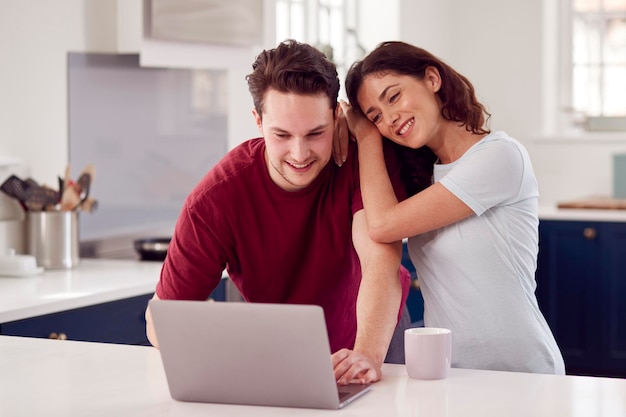 Couple transgenre aimant à la maison ensemble regardant un ordinateur portable sur le comptoir de la cuisine