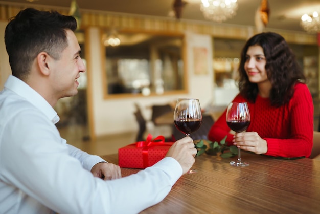 Couple trinquant avec du vin rouge Les amoureux s'offrent des cadeaux Beau dîner romantique