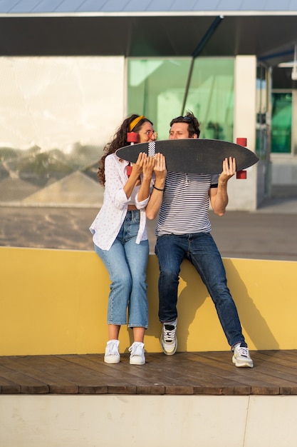 Un couple urbain à la mode profite de l'été dans un skate park en plein air s'assoit sur un longboard ludique et heureux