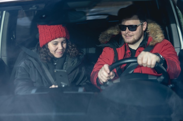 Couple en voiture en tenue d'hiver conduisant et parlant de la navigation au téléphone