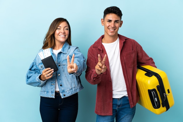 Couple de voyageurs tenant une valise sur bleu souriant et montrant le signe de la victoire