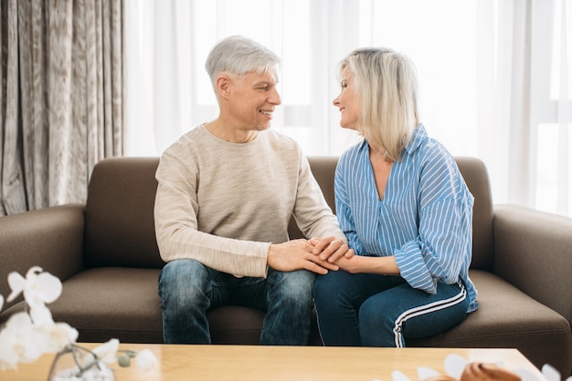 Les couples amoureux adultes se regardent dans les yeux à la maison. Mari et femme d'âge mûr assis sur le canapé et embrassant, famille heureuse