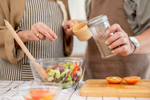 Des couples asiatiques heureux, mari et femme, cuisinent ensemble un bol de salade sain dans la cuisine.