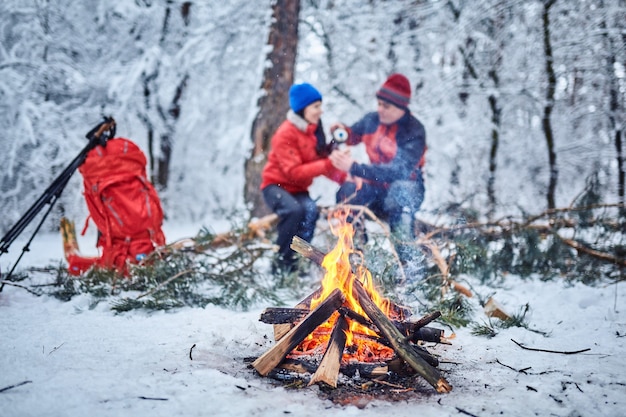 Couples heureux au-dessus d'un feu de camp dans la forêt enneigée d'hiver