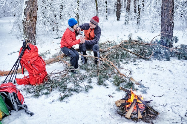 Couples heureux au-dessus d'un feu de camp dans la forêt enneigée d'hiver