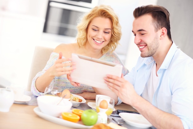 Couples heureux mangeant le petit déjeuner et utilisant le comprimé