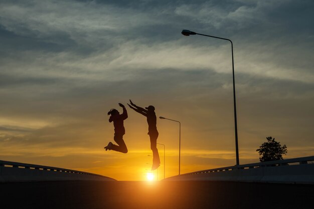 Couples de silhouette sautant au coucher du soleil