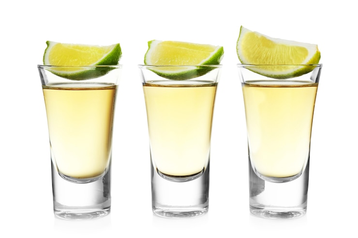 Photo coups de tequila d'or avec une tranche de citron vert d'affilée isolé sur blanc