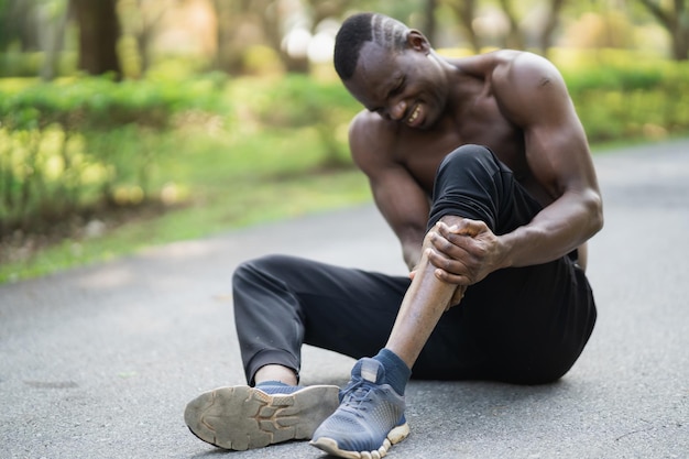 Un coureur africain assis sur une piste de jogging et ressentant une douleur dans l'espace de copie de sa jambe