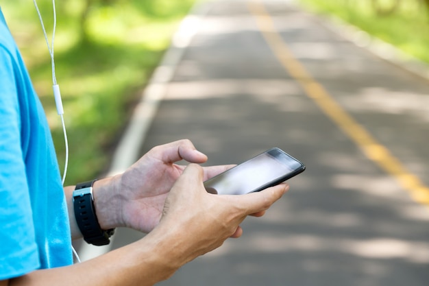 Coureur dans le parc à l'aide de smartphone sur une route