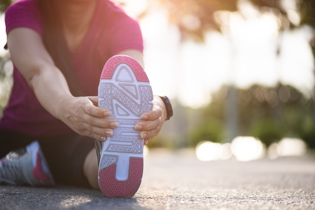 Coureur de femme assis sur la route qui s'étend de jambes avant de courir dans le parc.