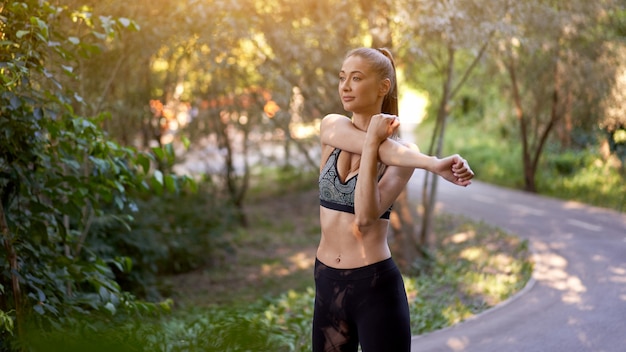 Coureur de femme s'étendant des bras avant d'exercer le matin de parc d'été